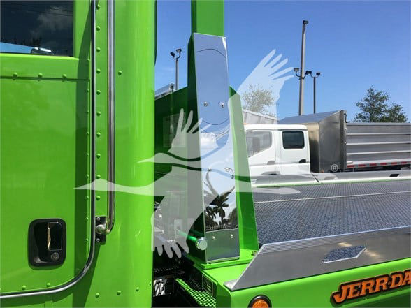 Green Peterbilt truck cab with chrome vertical component and rear step, visible yellow-orange 'JERR-D' lettering on a chrome plate, part of a tow truck bed.