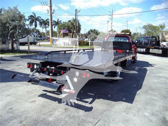 Tow truck teaser with a flatbed recovered in a lot. Visible text includes no legible stickers on the equipment in the image.
