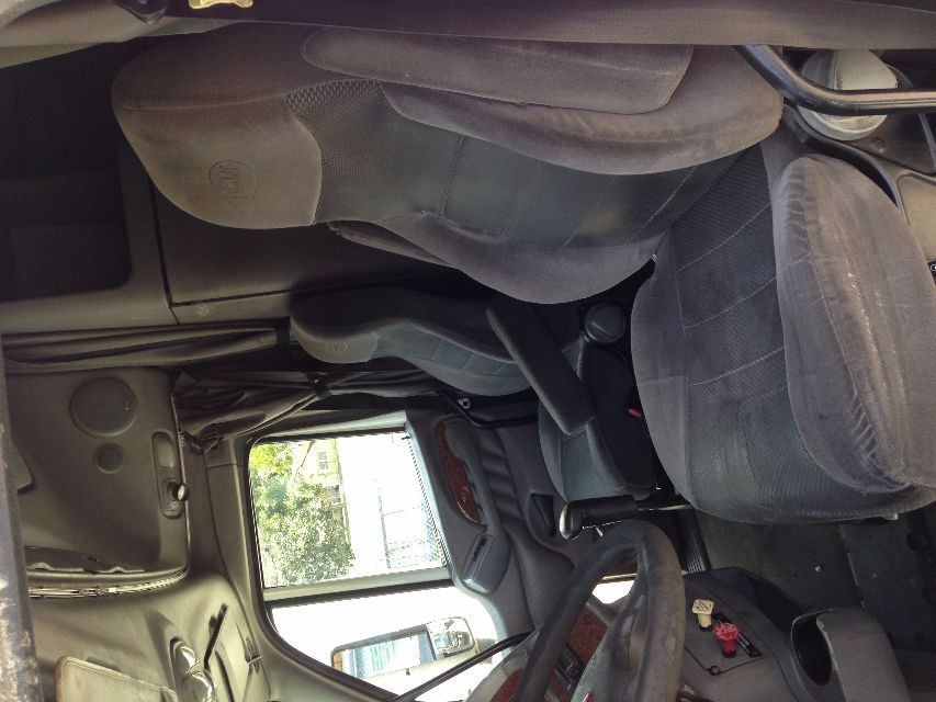 Peterbilt VN truck cab interior showing driver and passenger seats and steering wheel. Logos on seat, door panel, dashboard, and overhead storage area visible.