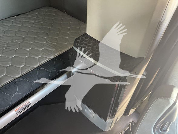 In-cab area of a Kenworth truck showing a sleeper bunk with quilted mattress and a side cabinet; no legible labels visible.
