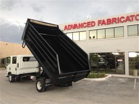 Dump truck with raised black dump body in front of Advanced Fabricators showroom.