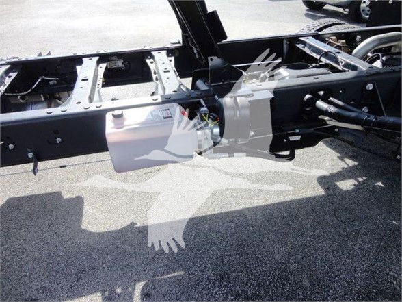 [Component] [View] showing a white plastic reservoir with a cap mounted to a vehicle frame, hydraulic lines nearby, chassis and frame rails visible.