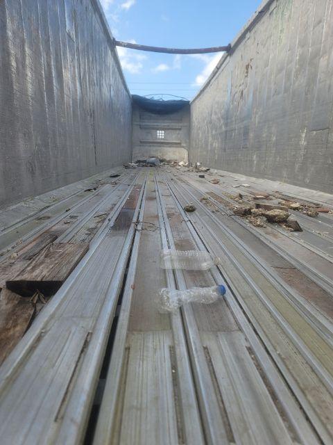 Interior of walking floor trailer bed showing metal floor with grooves and debris toward the far end.