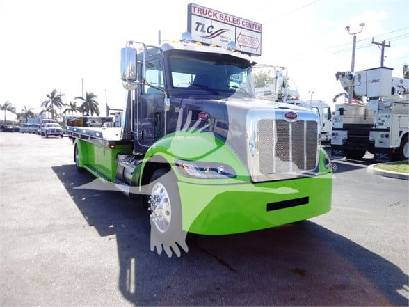 Peterbilt 337 tow truck with bright green front bumper and grille; large chrome grille, side mirrors, and stacked chrome exhaust; dealership lot in background.