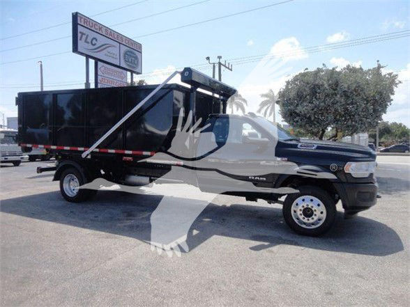 Ram 5500 HD refuse truck in a dealership lot with a large black dump body and white wheel hubs. Visible text on a sign in the background reads TLC and Truck Sales.