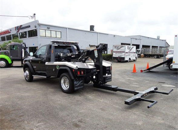 Tow truck with a black boom and wheel-lift attachment in a lot, 2024 Ram 4500 SLT displayed.
