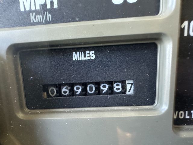 Instrument cluster showing odometer reading 690987 miles and partial speedometer/voltage gauges surrounding. The word MILES is visible above the odometer digits.