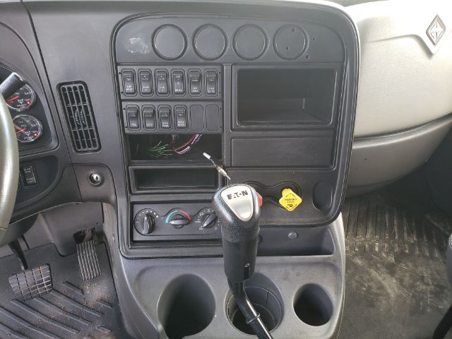Cab interior of 2015 International PROSTAR with steering wheel, dashboard switches, gear shifter, cup holders, and empty compartments; visible blank gauge cluster and loose wiring near center console.