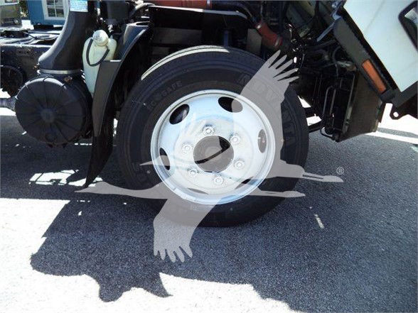 Isuzu NRR truck front wheel and axle area; visible tire with rim and surrounding components; watermark overlay of a bird-like logo. No legible serials or labels clearly readable.