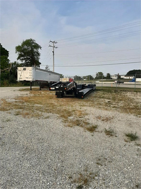 2023 Fontaine 55 ton steel lowboy trailer with a detachable gooseneck and flat deck, parked on gravel lot with chain-link fence in background.