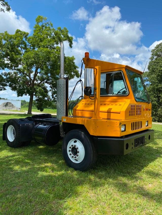 Orange Ottawa yard spotter 4x2 truck with tall exhaust stack and white wheels, on a grassy field under blue sky.