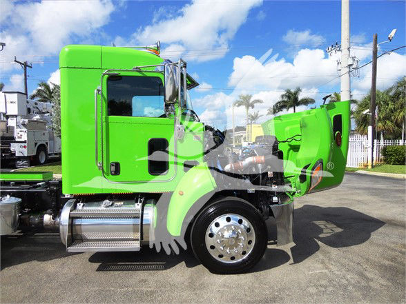 Green Peterbilt 337 truck side view showing bright cab and front wheel, empty sleeper area, chrome fuel tank, and lifted hood in an outdoor lot.