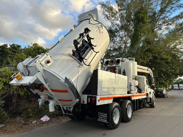 Vacuum truck 2016 International 7400 with large rear hopper tilted up, multiple axles, white with orange stripes, parked on street.