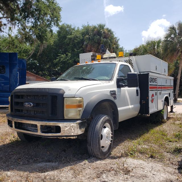 Ford F-550 utility truck in service with work body and rooftop lights, front left angle view showing grille, bumper, and utility storage compartments.