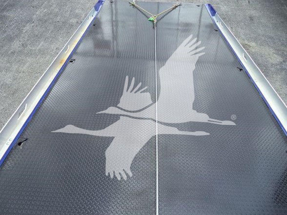 Truck bed surface with diamond plate pattern and a centered rope tie-down; partial reflection of a crane hook visible at top.
