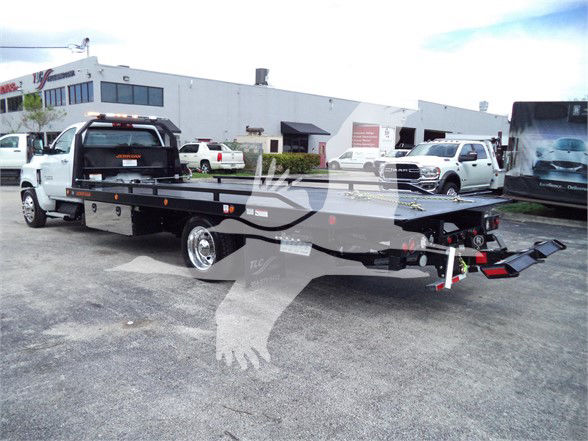 2023 Chevrolet Silverado 6500HD flatbed tow truck with extended flatbed and rear ramps, shown in a dealership lot.