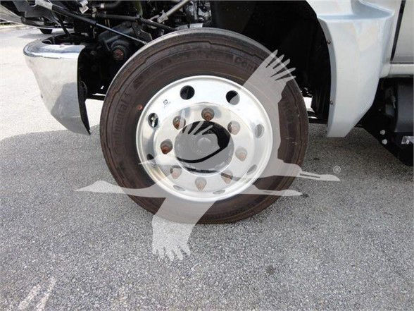 Truck wheel and tire on front-left of a 2023 Chevrolet Silverado 6500HD flatbed truck; chrome wheel with black tire, partial bumper and suspension visible.