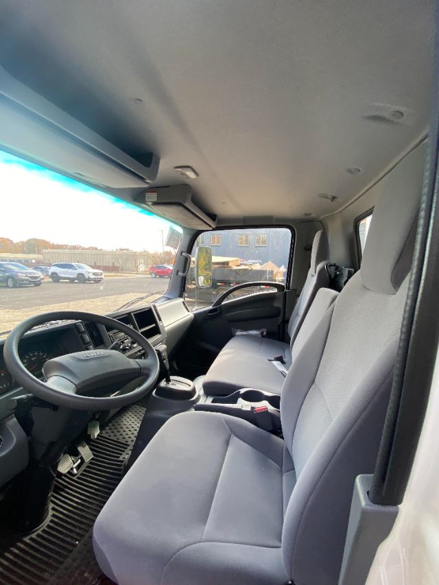Isuzu NRR cab interior showing gray cloth seats, steering wheel, dashboard, and driver area windshield with exterior lot.