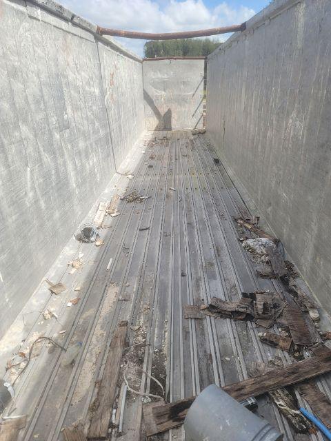 Trailer bed interior showing metal floor with debris and wood pieces, sidewalls, and open front gate.