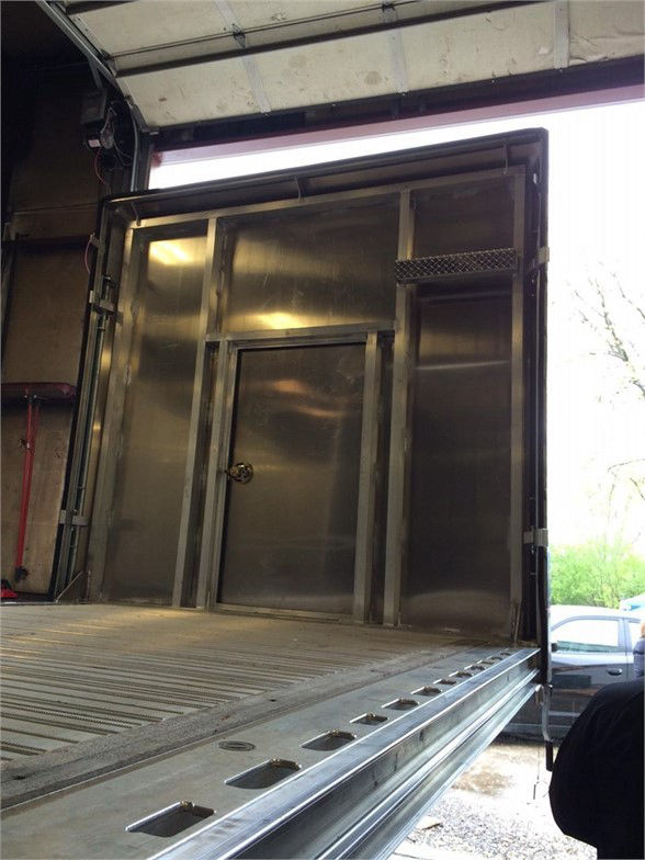 Trailer tarp system inside a Fontaine flatbed trailer with metal side walls and a ramp, showing rear entry and a doorway access with metal framing.