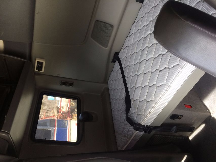 Interior sleeper cab of a 2011 International Prostar with a single bed, quilted mattress, window and seat belt visible; neutral gray panels surrounding the bed.