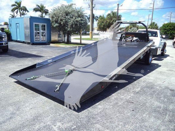 Flatbed tow truck trailer on a white Ram 5500 chassis with a long black steel platform and winch trolley, in an outdoor lot.