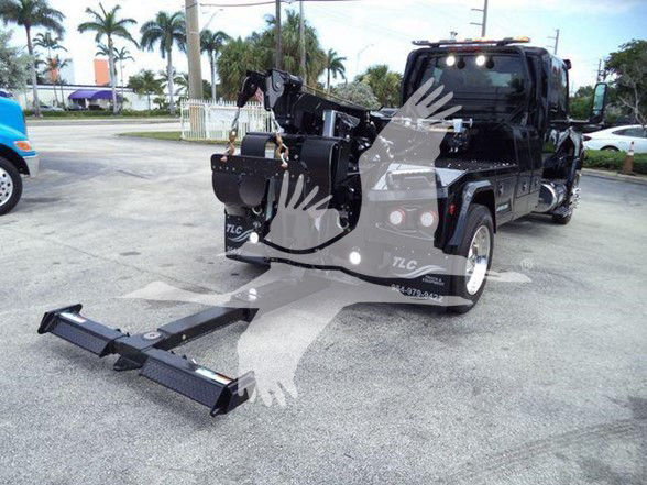 Tow truck with hitch extension and crane equipment in rear view, International MV series likely in dealership lot.