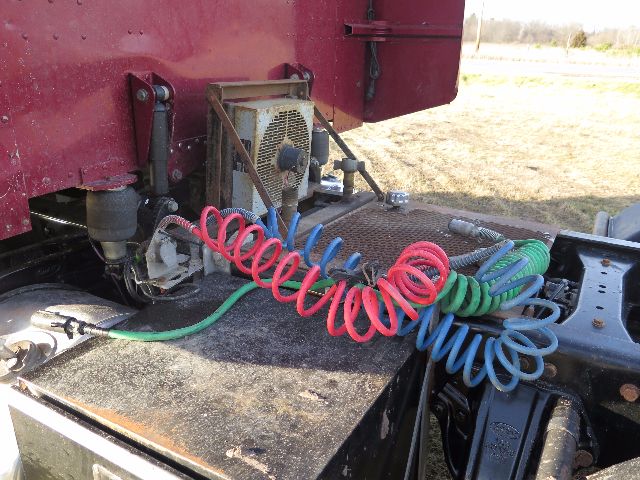 Air system and cables with coiled red, blue, and green hoses on a Peterbilt truck chassis; small radiator grille and fan visible; dirty metal surface.