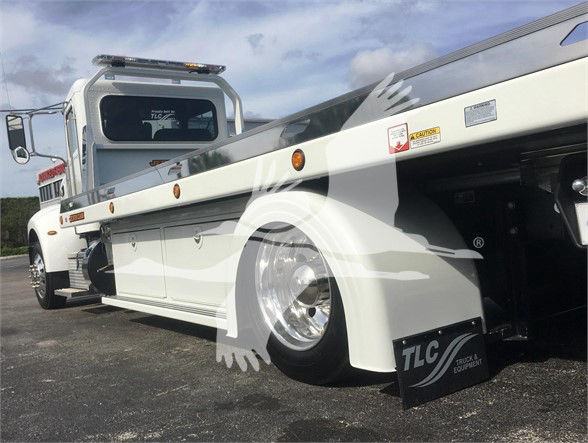 Peterbilt 337 tow truck side view with white body, black trim, and a low-profile chassis. Visible text includes TLC Truck & Equipment on a black front fender mudflap and a small warning sticker near the cab.
