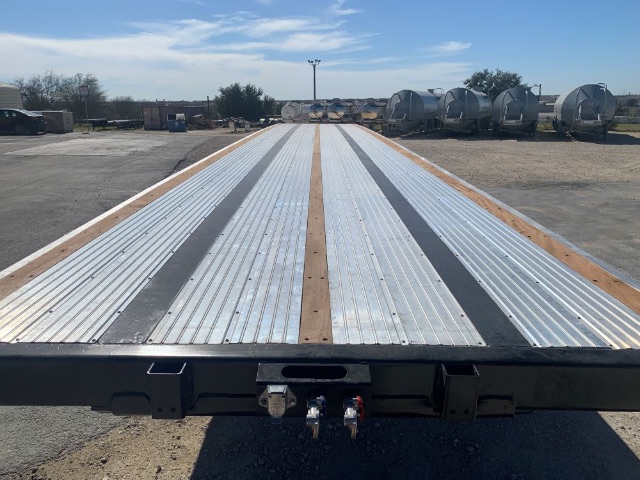 48ft flatbed trailer bed with corrugated aluminum decking and wooden center strips, rear connection fittings visible, industrial yard background