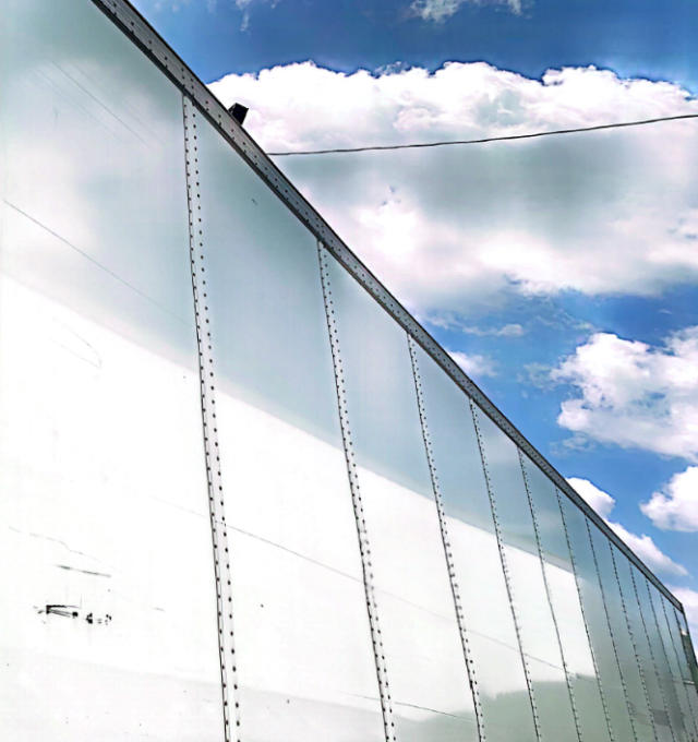 2018 Vanguard VXP trailer side panel showing smooth aluminum exterior with vertical rivet seams and blue sky background.