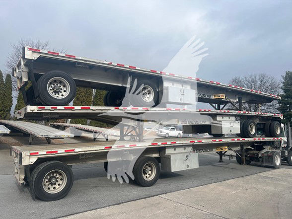 Flatbed trailers stacked in a yard, two-level car hauler with multiple axles and wheels visible, Benson branding on side rails.
