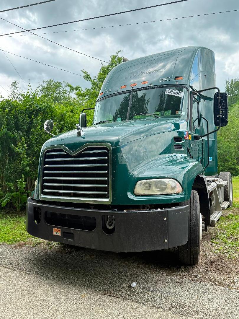 Conventional daycab truck front view 2016 Mack CXU 612 with green paint, large grille, chrome mirrors, and black bumper. Visible windshield stickers and dual headlights.