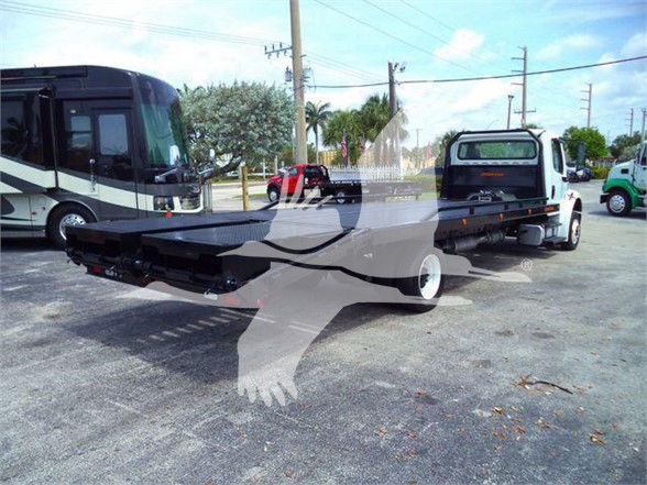2012 Freightliner BUSINESS CLASS M2 106 flatbed truck with a long flatbed and wheel-lift tow hitch in a parking lot.