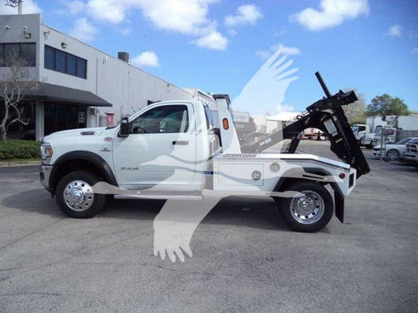 2024 Ram 5500 SLT tow truck, white single-cab with a hydraulic bed hoist, visible RAM badge on front fender, doors, and wheel covers. Background shows dealership lot.