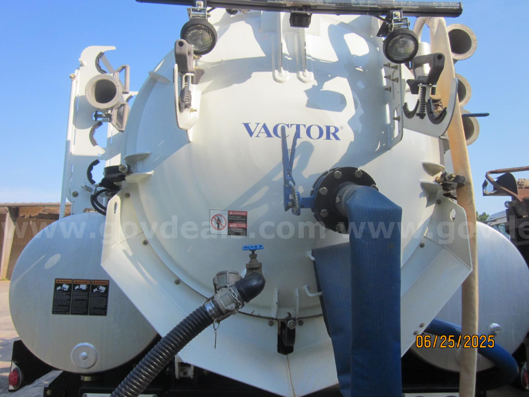 Vactor truck vacuum tank rear view with hoses and blue inlet hose, Vactor logo on tank, warning labels, date stamp.