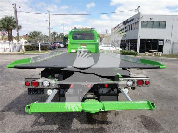Tow truck rear view with green metal hitch and loading platform, dual rear lights, and bumper, with MV607STEPSIDEFM stock building in background.