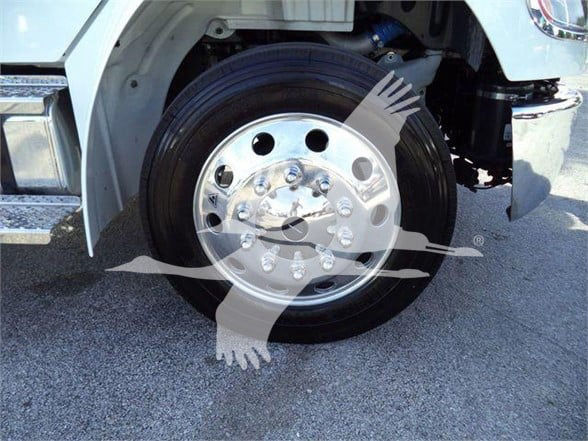 Freightliner truck wheel and tire with shiny aluminum hubcap; partial front wheel well and suspension visible.