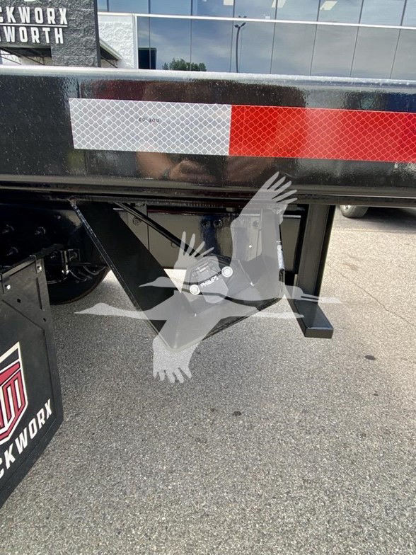 Kenworth T480 flatbed truck rear undercarriage showing reflective red/white marker and landing gear area.