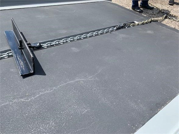 Container delivery trailer deck with chain and hitch component visible on a flat black surface.