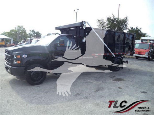 2019-2023 Chevrolet Silverado 6500HD dumping truck in a dealership lot with TLC Truck & Equipment watermark. Visible text includes 'TLC Truck & Equipment' logo and faint background signage.