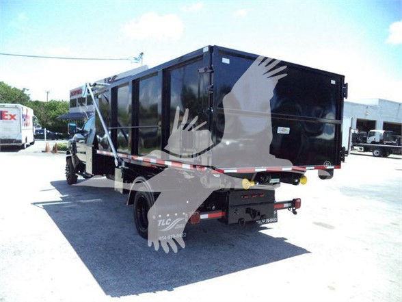 Black garbage truck body mounted on a medium-duty truck chassis, side view showing refuse bin and hydraulic system, tail area with bumper and hitch.