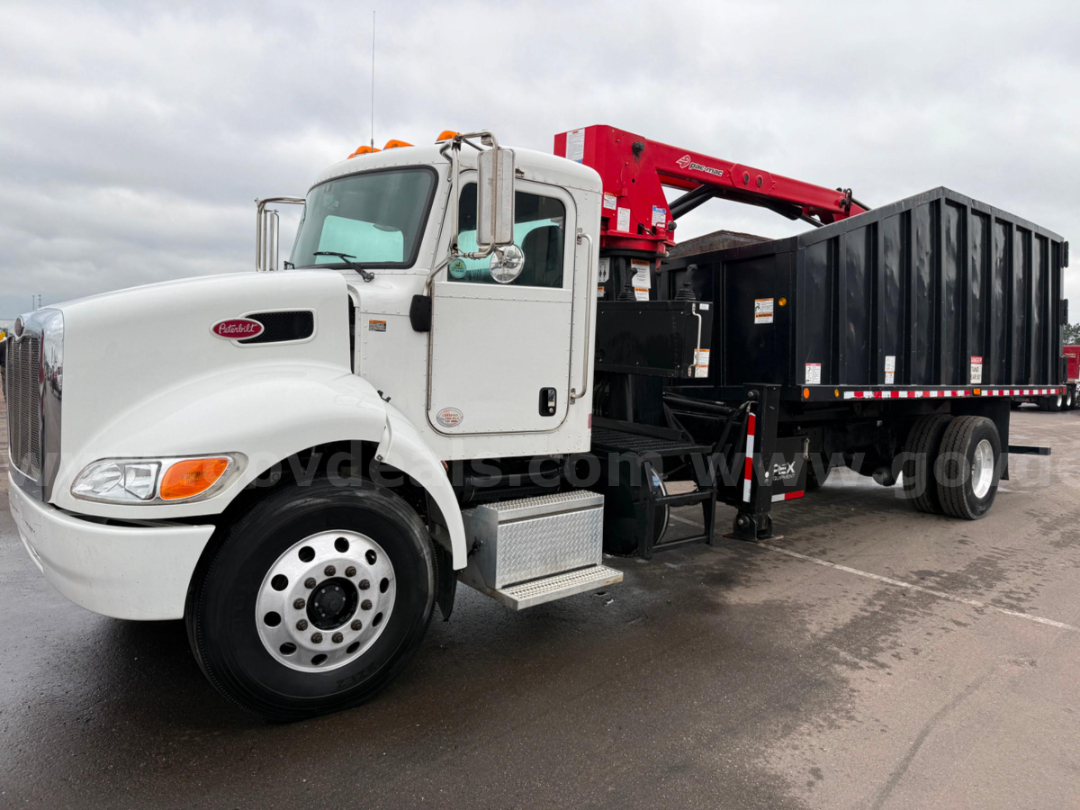 Peterbilt truck with a red Pac-Mac KBF-20H grapple crane and a black dumping bed. Front wheel visible, white cab, orange lights on top.
