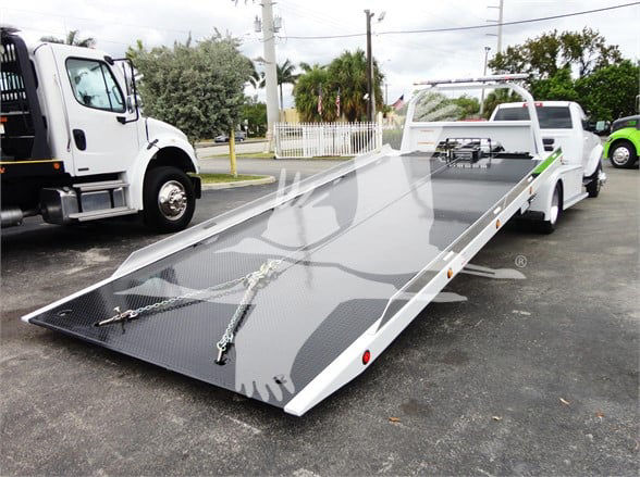 Ram 5500 forward view showing a long flatbed tow truck bed with winch hooks and metallic diamond plate surface.
