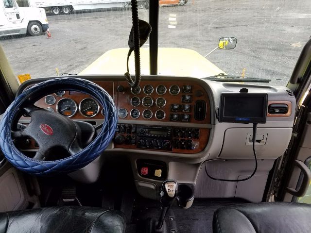 Peterbilt truck interior dashboard with steering wheel and numerous gauges, woodgrain panel, and gear shifter.