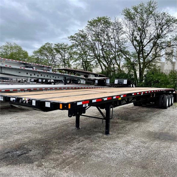 Flatbed trailer in a yard showing extended all-steel frame with wooden deck and extendable middle section, Fontaine XCALIBUR style, 53-90 feet length, dual rear axles.
