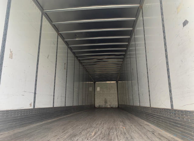 Trailer interior showing long empty cargo area with ribbed walls and ceiling, rear door closed, light from front opening.