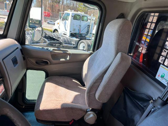 Truck cab interior showing driver's seat and passenger seat, with door panel and window. Outside, another truck is visible in the lot.