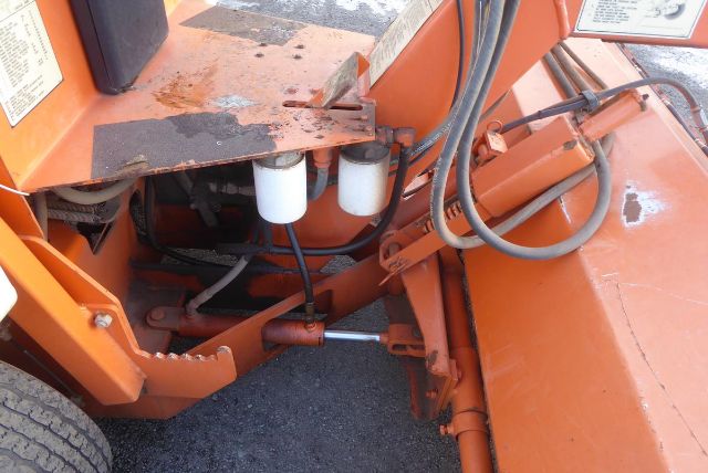 Trucking equipment showing hydraulic hoses, white cylindrical filters, and orange metal frame near cab area.