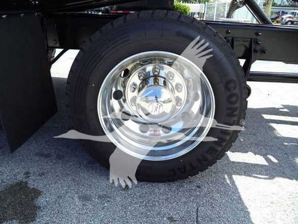 Wheel and tire assembly on a trailer chassis with chrome hub cap and treaded tire.